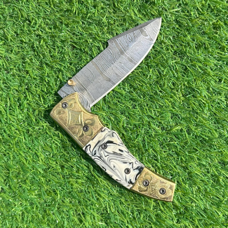 Damascus folding knife closed showing intricate brass engravings and marbled handle pattern