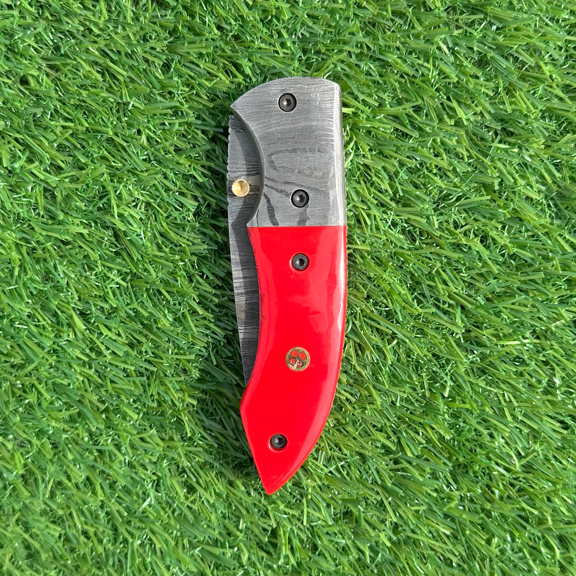 Damascus folding knife red handle closed showing brass accents and Damascus bolsters