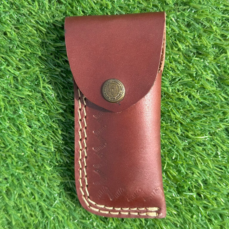 Hand forged Damascus steel folding knife with red pakkawood handle closed position on grass