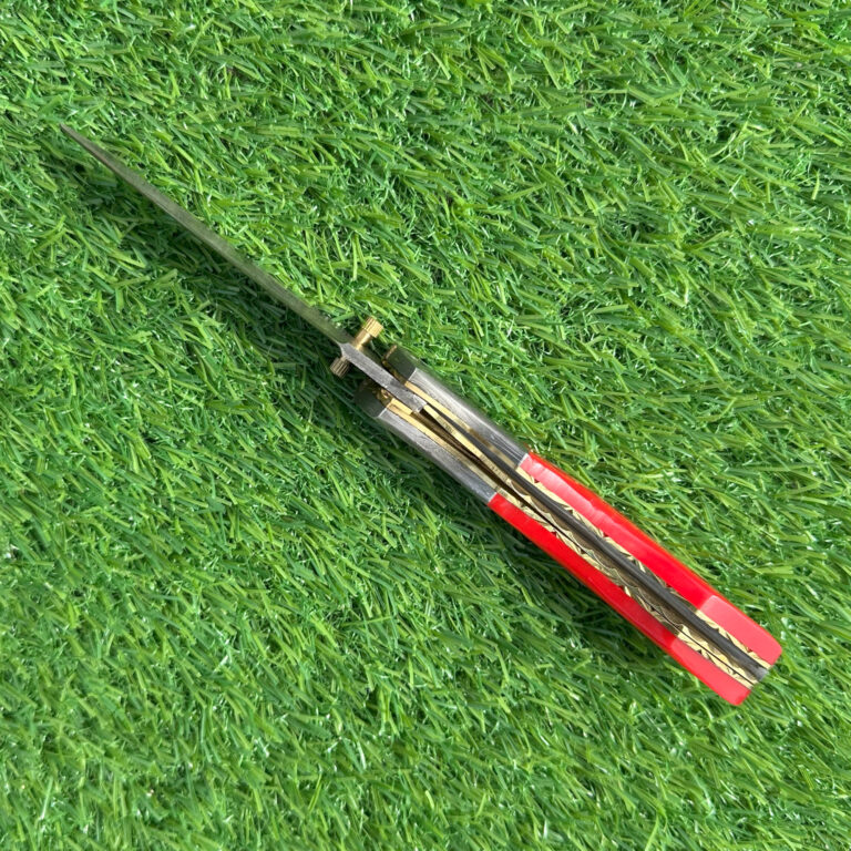 Side view Damascus pocket knife displaying blade pattern and red handle detail